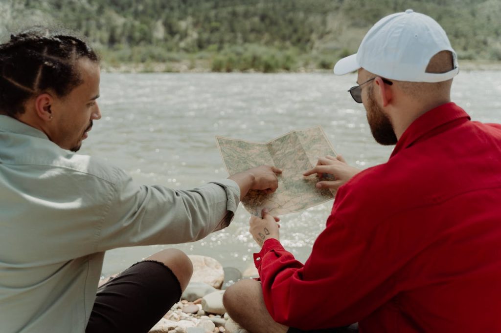 Two men study a map by a calm river, planning their next adventure.