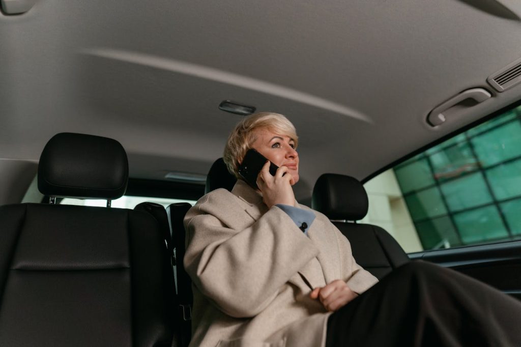 A woman in a brown coat making a phone call while sitting in a car.