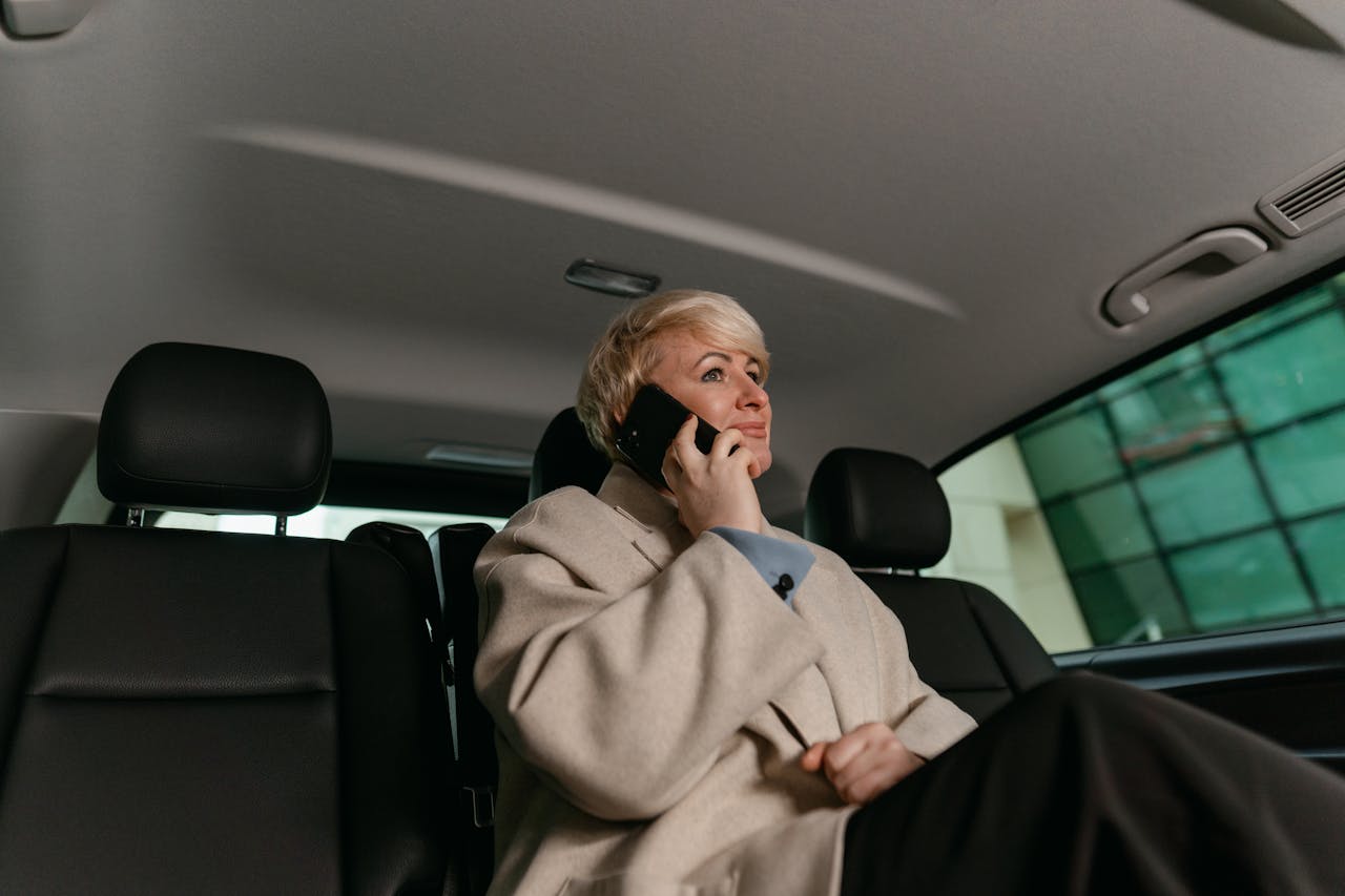 A woman in a brown coat making a phone call while sitting in a car.